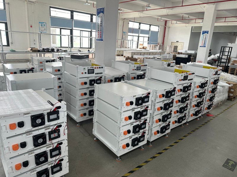 Stacked rows of modular high-voltage lithium battery cabinets and rack-mount units inside an industrial manufacturing factory, showcasing compact footprint and high power output design.