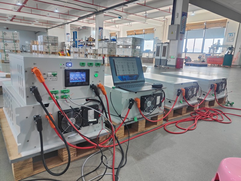 Rakour high-voltage battery control unit (BCU) connected with heavy-duty cables, undergoing real-time system monitoring and laptop debugging in a testing facility.